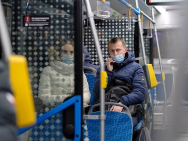 Yüz maskeli genç bir adam şehir otobüsünde oturuyor ve telefonla konuşuyor..
