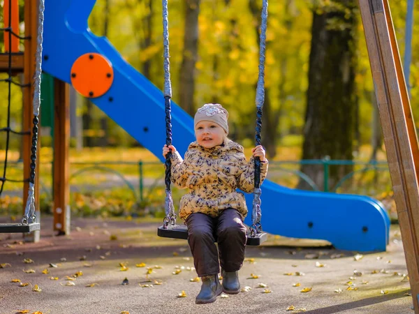 Bayi perempuan duduk di ayunan di taman bermain di sebuah taman musim gugur. — Stok Foto