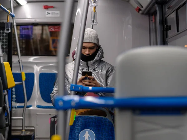 Een jongeman in een stadsbus kijkt aandachtig naar het smartphone scherm. — Stockfoto