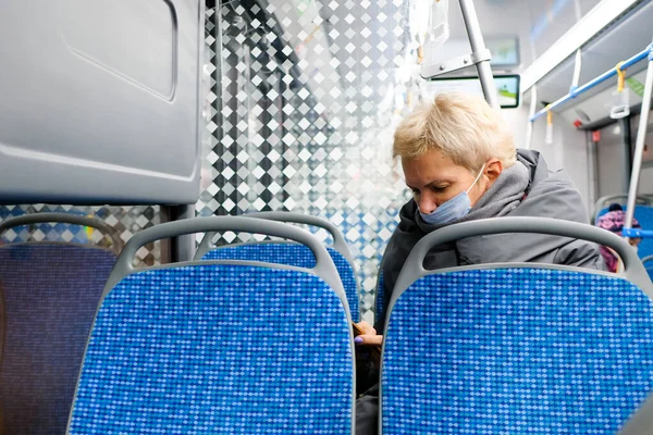 Een vrouw met een medisch masker met een smartphone in haar hand zit in de bus. — Stockfoto