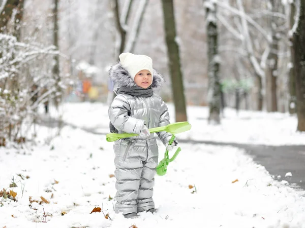 Una bambina divertente in una tuta argentata calda tiene una pala giocattolo. — Foto Stock