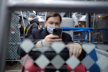 Maskeli bir adam otobüste akıllı telefon kullanır..