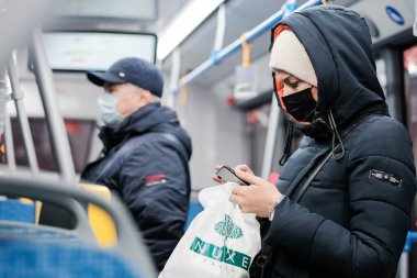 Otobüste koruyucu maske takan genç bir kadın akıllı telefon kullanıyor..