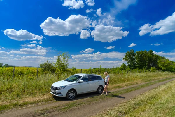 Chica bebe café cerca de un coche blanco en un fondo de cielo azul con nubes. — Foto de Stock