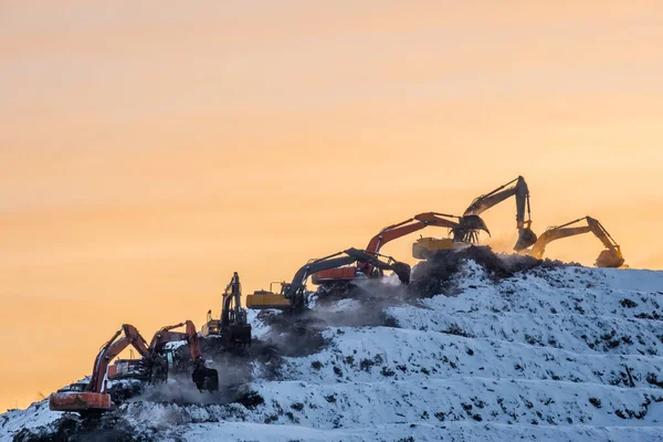Siluetas de muchas excavadoras trabajando en una enorme montaña en un basurero — Foto de Stock