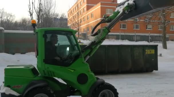 Pequeños cargadores frontales limpian la nieve de la calle y la cargan en un búnker. — Vídeos de Stock