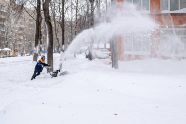Bir kamu görevlisi kar yağışı sırasında makina güdümlü kar küreme aracı ile bir yolu temizliyor.