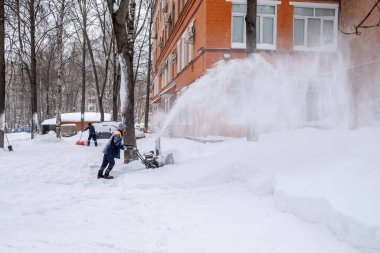 Bir kamu görevlisi kar yağışı sırasında makina güdümlü kar küreme aracı ile bir yolu temizliyor.