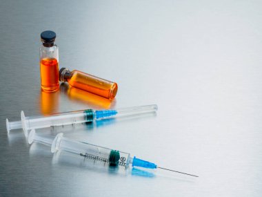 Alüminyum zemin üzerinde turuncu koronavirüs aşısı olan şırıngalar ve ampuller.. 