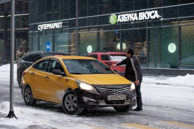 Bir taksi şoförü ön camı silecek fırçaları ve buzu temizler..