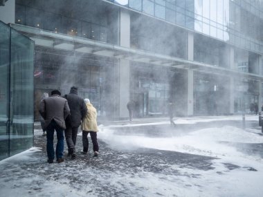 İnsanlar yoğun bir kar yağışı ile birlikte bina boyunca yürürler..