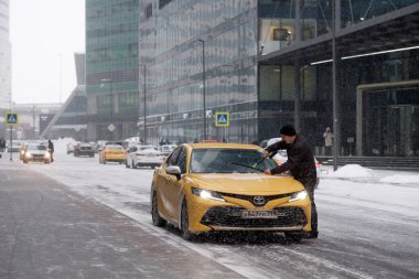 Bir taksi şoförü ön camı silecek fırçaları ve buzu temizler..