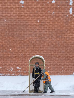 Bir kamu görevlisi Kremlin duvarının yakınındaki bir karakolda askerin yanında kar temizliyor..