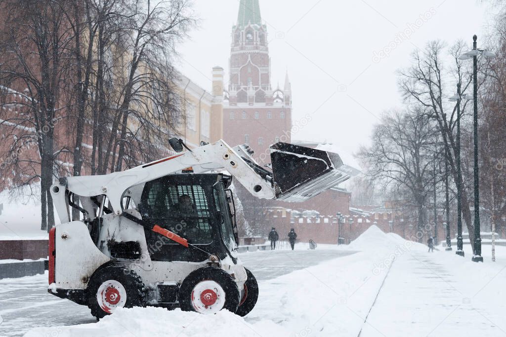 A small loader excavator bobcat removes snow from the sidewalk near the Kremlin walls during a heavy snowfall. 
