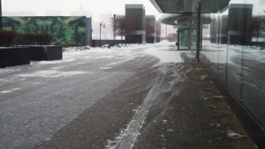 Rüzgârla taşınan kar, cam cepheli, bilinmeyen modern bir binanın yakınındaki kaldırımda ilerliyor. Kış günü. Şehirde kar yağışı. Yüksek kalite 4k video