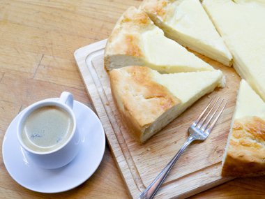 Üçgen dilimli ekşi turtaya yakın plan - ulusal bir Tatar yemeği. Tost kenarlı, ahşap bir masa ve beyaz seramik kahve fincanı ve çatallı büyük ev yapımı cheesecake..