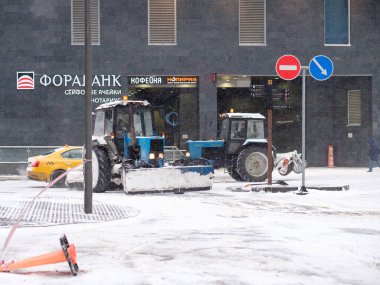 Moskova. - Rusya. 12 Şubat 2021. Elinde kova ve mekanik bir fırça olan bir traktör kar yağışı sırasında şehirdeki bir caddede kar temizler. Tekniği kalın bir kar tabakasıyla kaplı..