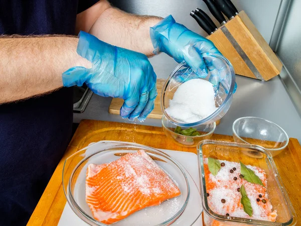 The gloved cook sprinkles the salmon fillet with curing mixture. — Stock Photo, Image