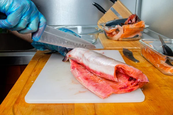 Руки кухаря в рукавичках вирізали тіло рожевого лосося ножем . — стокове фото