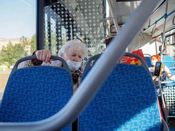 Старая седовласая женщина в защитной маске сидит у окна городского автобуса. — стоковое фото