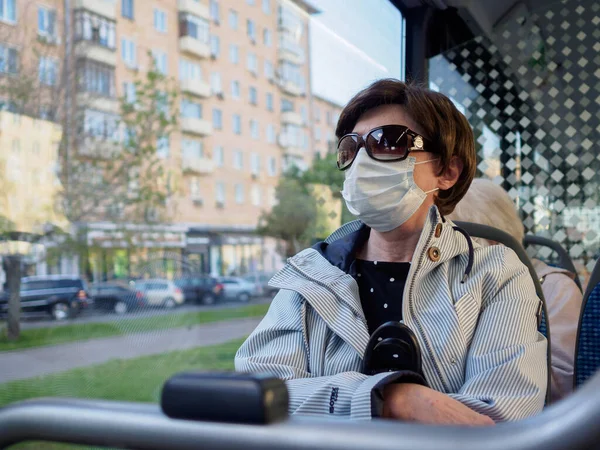 Взрослая женщина в маске и солнцезащитных очках сидит у окна в городском автобусе — стоковое фото