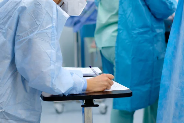 Una doctora toma notas en documentos durante la cirugía. — Foto de Stock