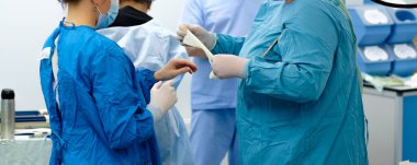 Bir asistan, bir kadının steril lateks eldiven giymesine yardım eder..