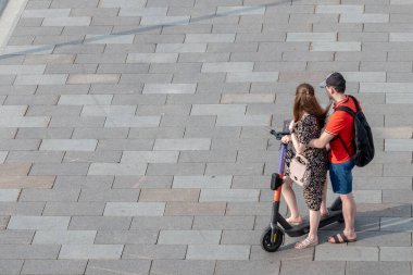 Bir kız ve bir erkek aynı elektrikli scooter 'da birlikte duruyorlar.