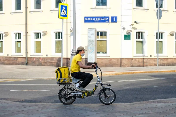 Ein Essenslieferant fährt mit einem Elektro-Fahrrad eine Stadtstraße entlang. — Stockfoto