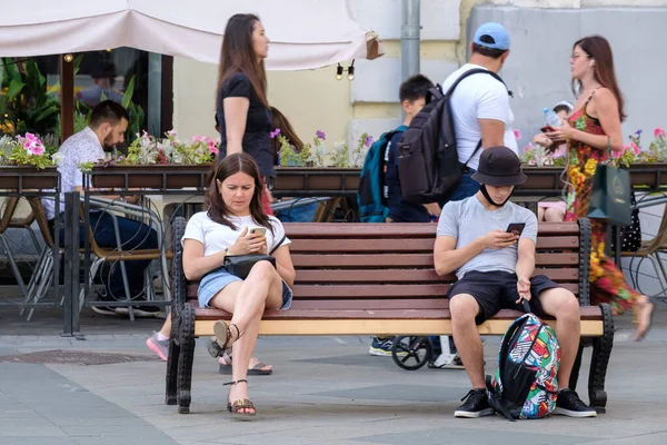 Молодой человек и женщина сидят на скамейке и печатают на мобильных телефонах. — стоковое фото