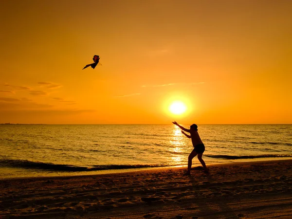 Egy lány sárkánnyal játszik naplementekor a tengerparton.. — Stock Fotó