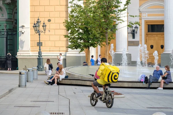Ένας διανομέας τροφίμων οδηγεί ένα ηλεκτρικό ποδήλατο κατά μήκος ενός δρόμου της πόλης. — Φωτογραφία Αρχείου