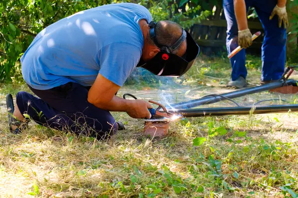 Seorang Pekerja Yang Mengenakan Topeng Pelindung Mengelas Pipa Logam Dengan — Stok Foto