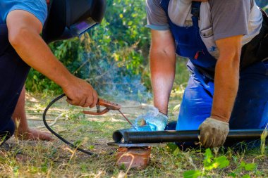 İşçiler metal borulara elektrik kaynağı döşüyorlar.