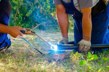 Metal boruları elektrik yayı ile kaynak yapan işçilerin elleri.