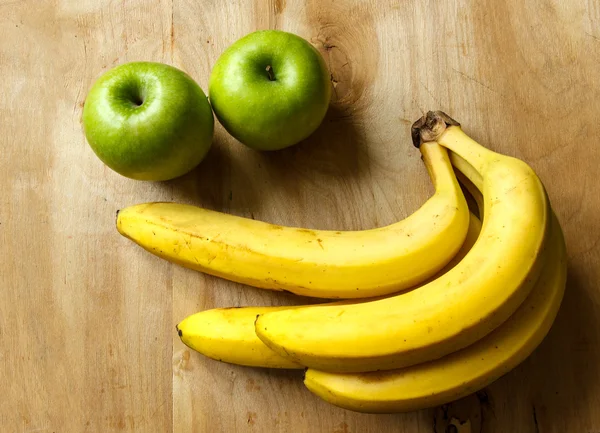 Натюрморт Два зеленых яблока и куча спелых бананов на деревянном фоне — стоковое фото