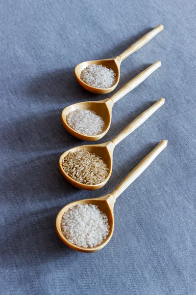 Wooden spoons with different kinds of rice on a gray woven background - basmati, brown, long grain white and round white