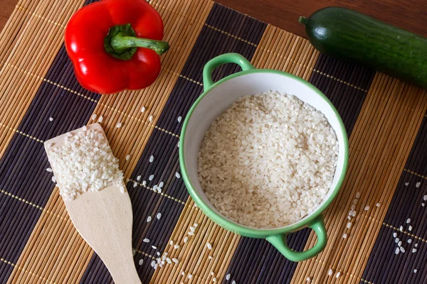 Bowl with rice, wooden shovel, red pepper and cucumber on a bamboo mat — Stock Photo, Image