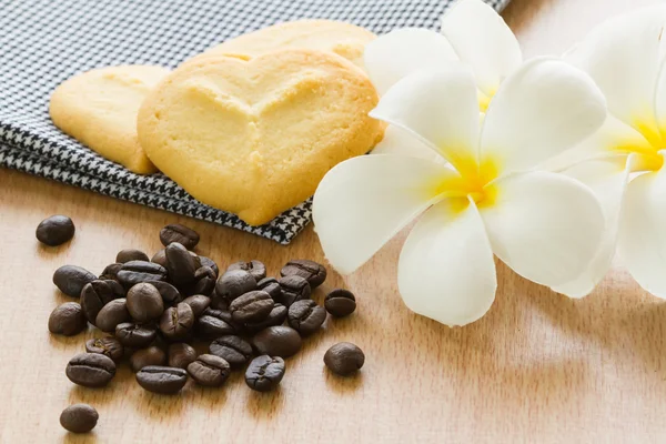 Coffee grains with cookie and plumeria flower. — Stock Photo, Image