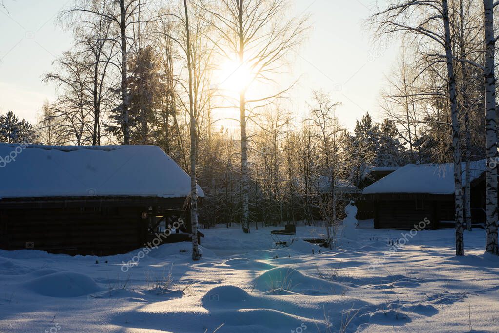 wooden house in the winter snowy forest and the sun