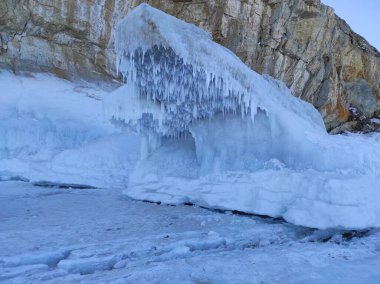 Karla kaplı kayalar ve buzla kaplı gölün yakınındaki sarkıtlar.