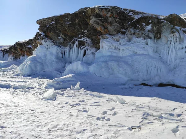 Rotsen bedekt met sneeuw en ijspegels in de buurt van een meer bedekt met ijs — Stockfoto