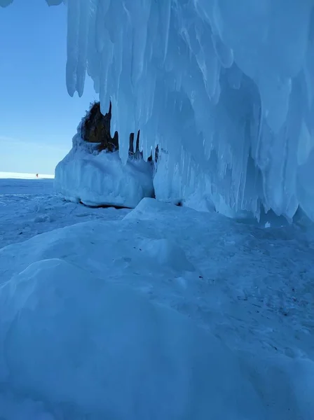 被雪覆盖的岩石和冰柱靠近被冰覆盖的湖面 — 图库照片