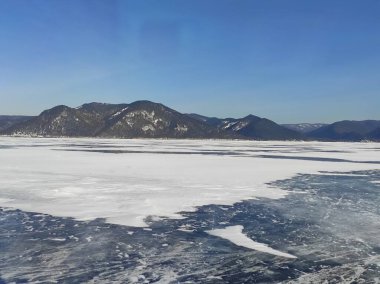 Kışın, kar kaplı dağların arasında, gölün şeffaf mavi buzu.