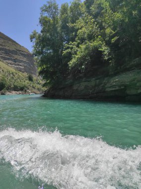 Mavi nehri olan derin bir kanyon ve mavi gökyüzüne karşı güzel dağlar.