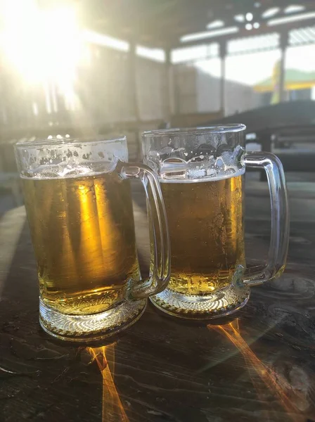 Duży kubek piwa stoi na stole w promieniach słońca — Zdjęcie stockowe