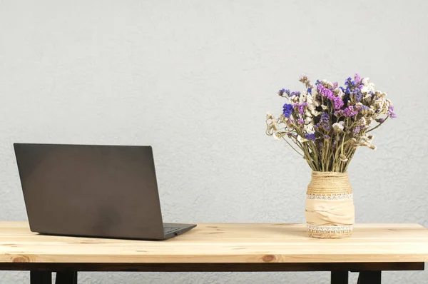 Open laptop and a vase of flowers on a wooden table.