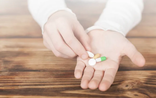 Pills in hand. Patient illness concept. On a wooden background