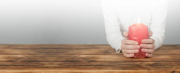 Lighted candle in hands. On a wooden background. Christmas. Copy space