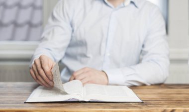 İncil 'i aç. Adam kitabın sayfalarını kurcalıyor. Masada oturmuş kitap okuyor..